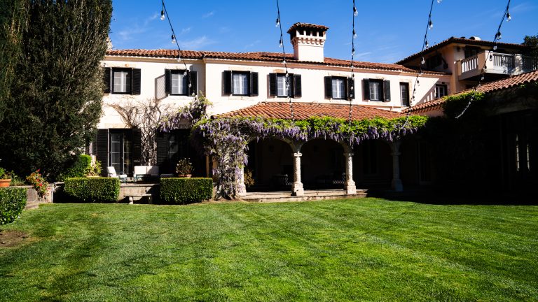Front of Stone Pine Estate, a wedding and events venue in Carmel, CA. Pictures shows the outside of part of the estate, featuring a green, manicured and properly fertilized lawn.