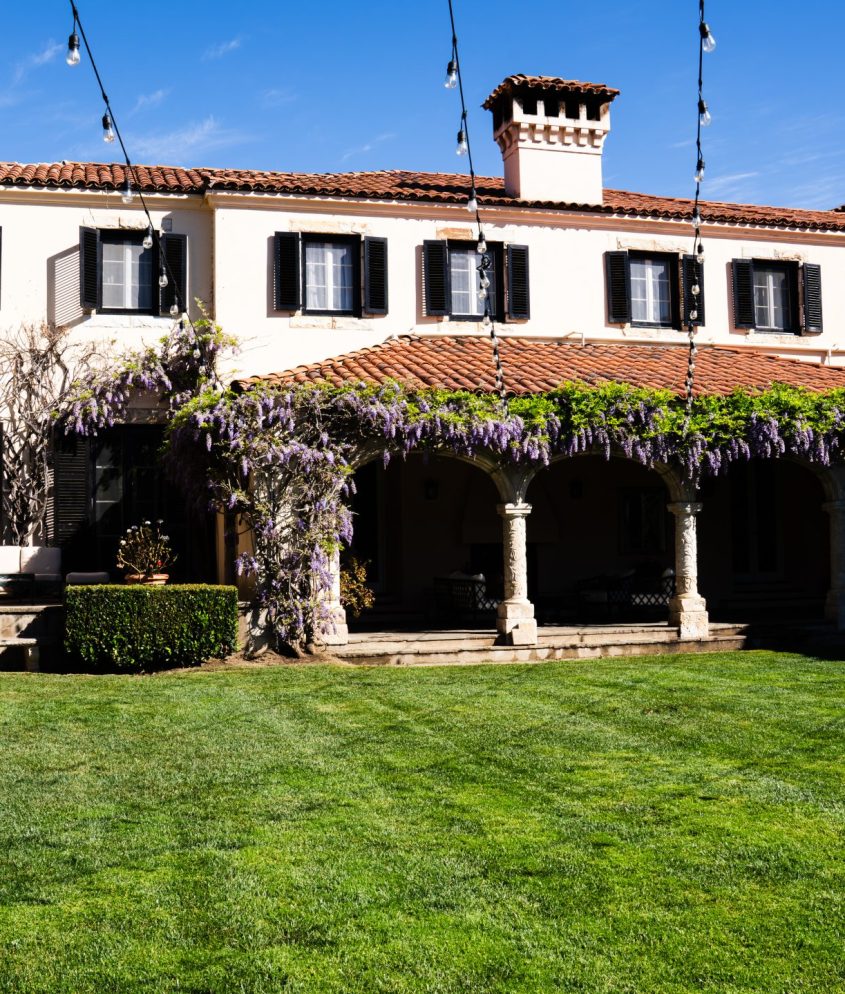Front of Stone Pine Estate, a wedding and events venue in Carmel, CA. Pictures shows the outside of part of the estate, featuring a green, manicured and properly fertilized lawn.